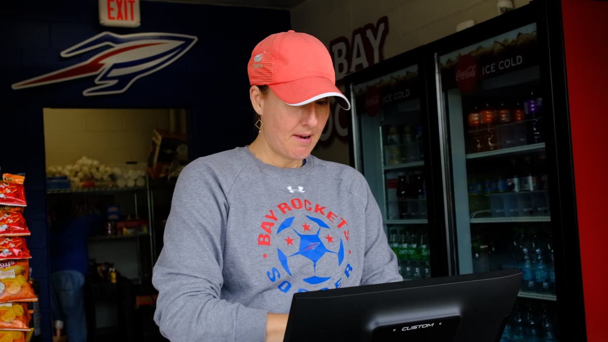 A volunteer in a team sweatshirt working the terminal inside a concession stand