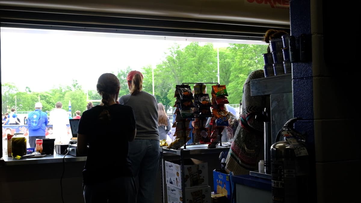 Volunteers behind the counter of a school concession stand, looking out at the field on a game day