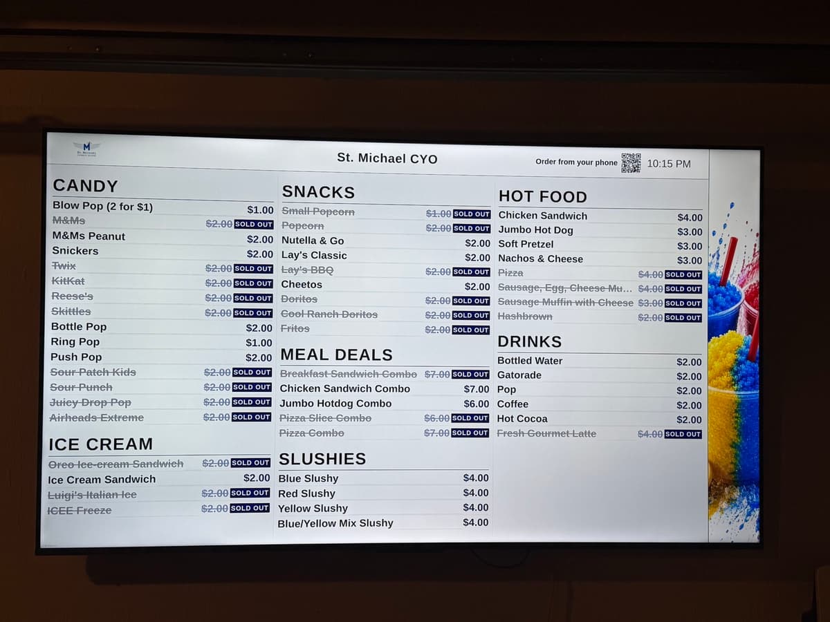 A BlazeBite menu board on a TV at a school stand, with prices and sold-out items struck through