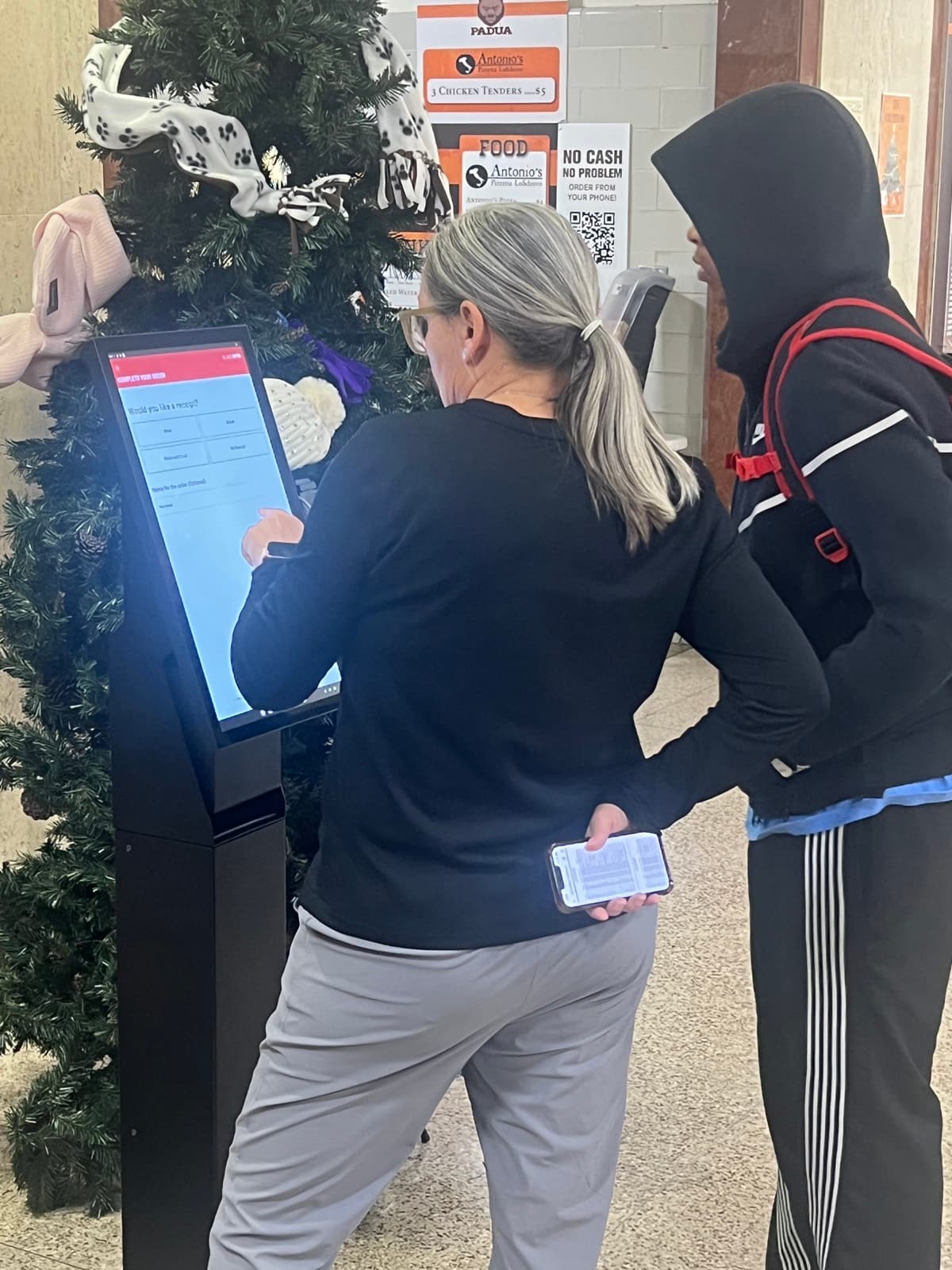 A customer tapping through the menu on a BlazeBite kiosk, phone in hand